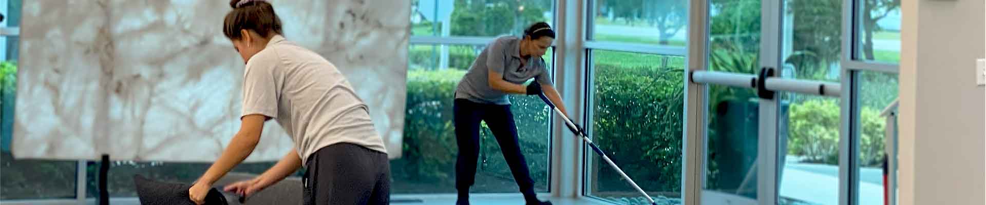 Two professional cleaners dusting furniture in a modern office lobby